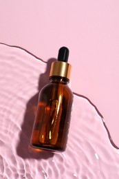 Bottle of cosmetic oil in water on pink background, top view