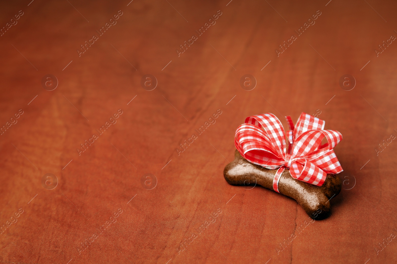 Photo of Bone shaped dog cookie with red bow on wooden background, space for text