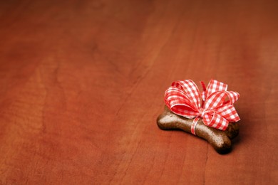 Photo of Bone shaped dog cookie with red bow on wooden background, space for text