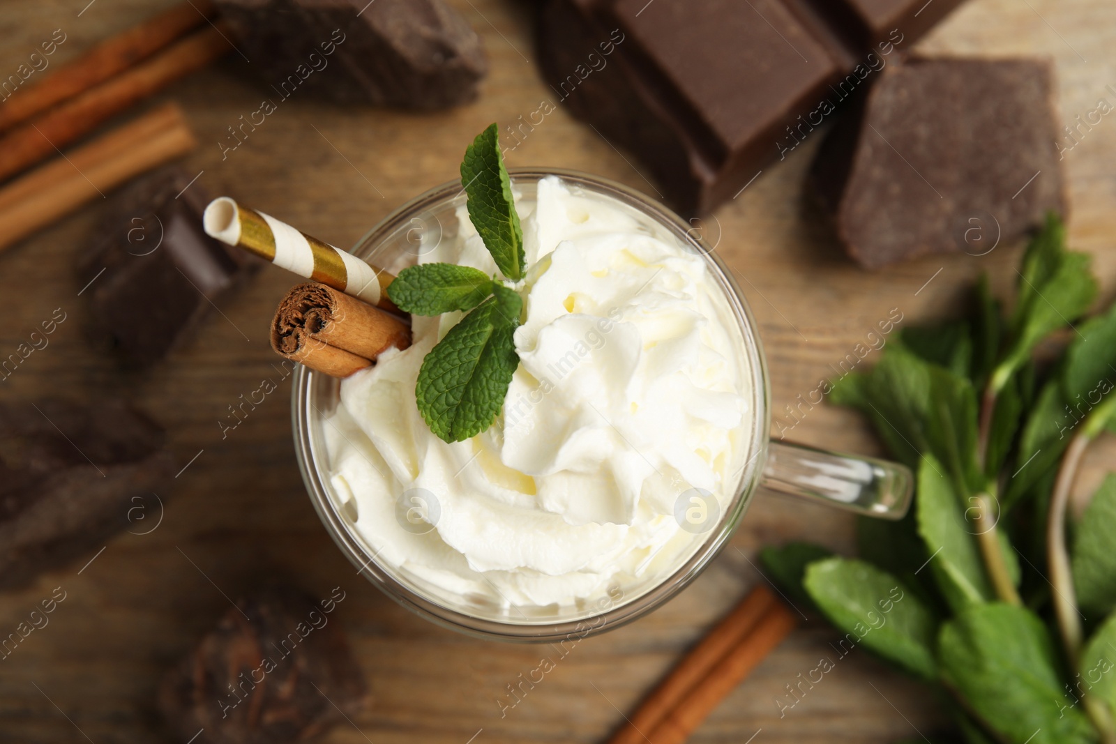 Photo of Glass cup of delicious hot chocolate with whipped cream and mint on wooden table, flat lay