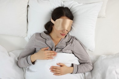 Young woman with sleeping mask in bed, top view