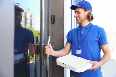 Male courier with pizza at entrance. Food delivery service