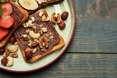 Photo of Tasty toasts with chocolate spread, nuts, strawberries and banana served on wooden table, top view. Space for text