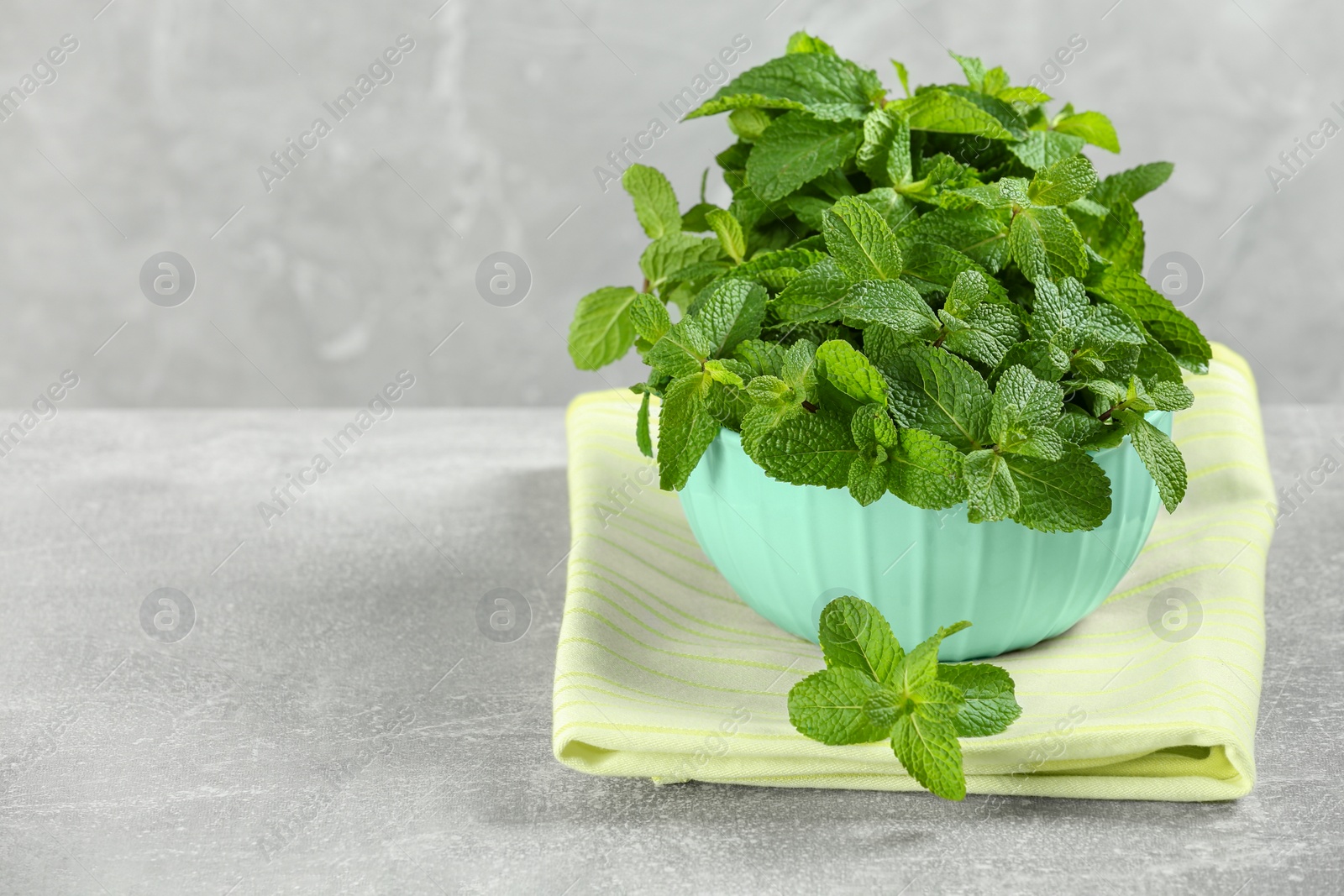 Photo of Bowl with fresh green mint leaves on grey table. Space for text