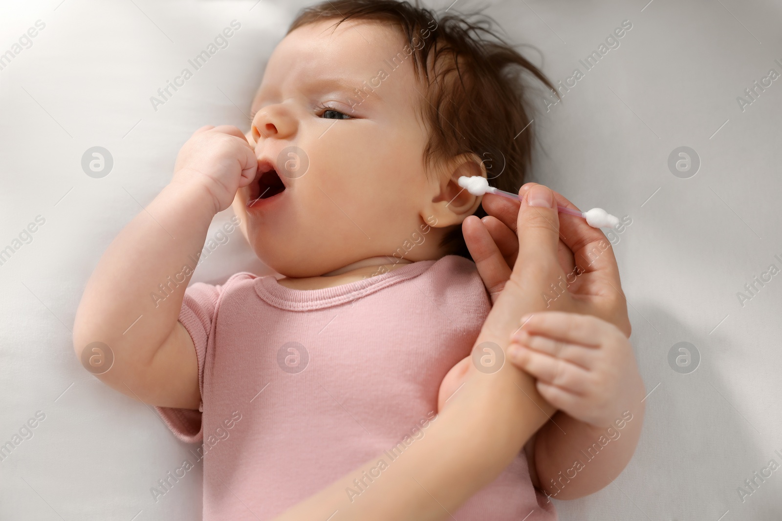 Photo of Mother cleaning ears of her baby with cotton bud on bed, closeup