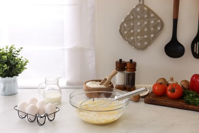 Photo of Metal whisk, cream in bowl and different products on light table indoors