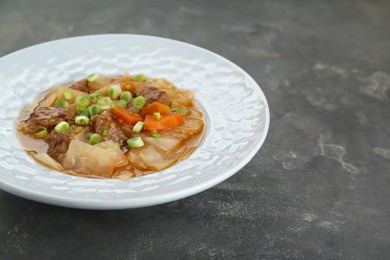 Photo of Tasty cabbage soup with meat, green onion and carrot on grey table, closeup. Space for text