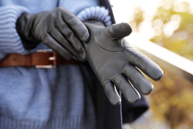 Photo of Young woman putting on stylish black leather gloves outdoors, closeup