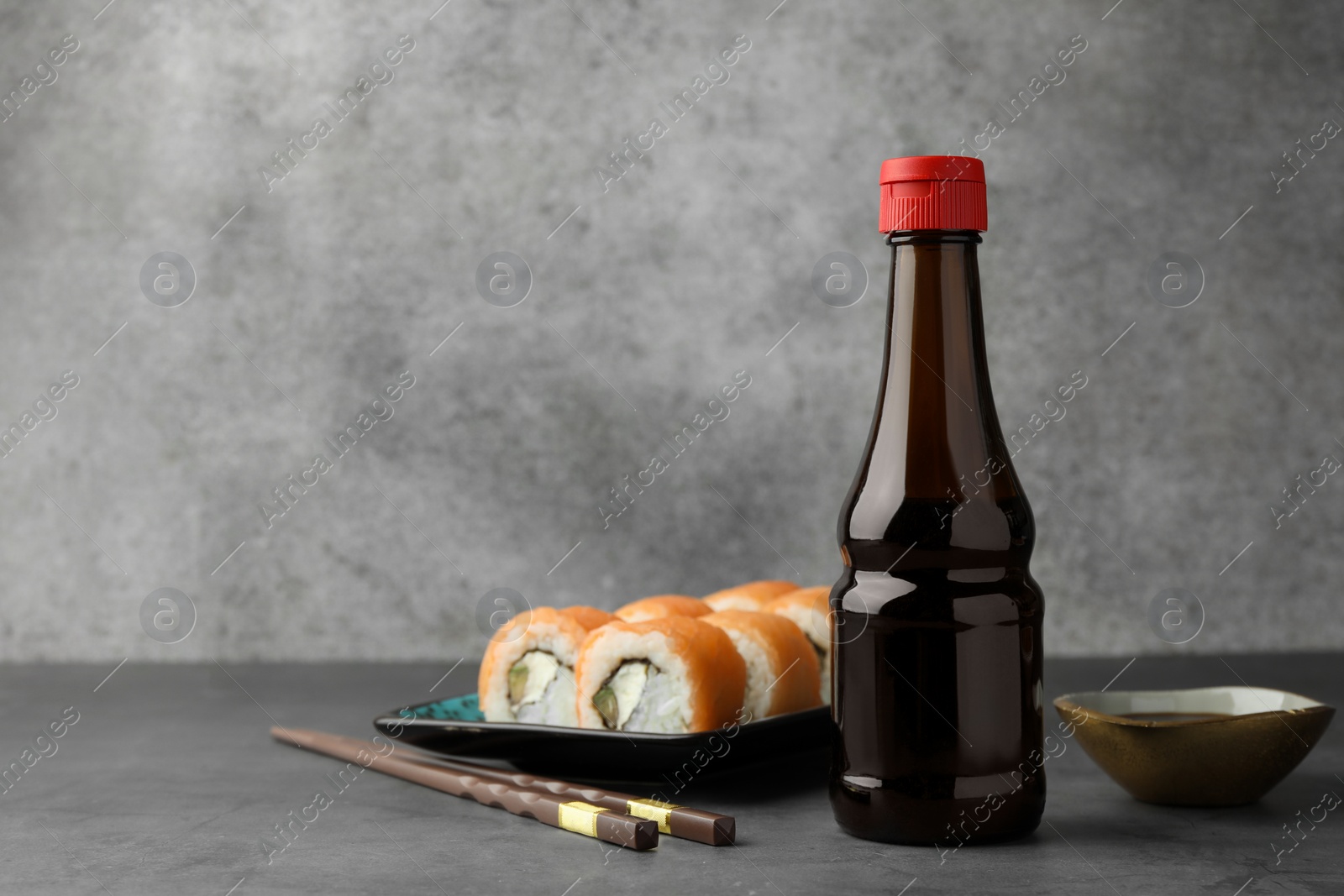 Photo of Tasty soy sauce, chopsticks and sushi rolls with salmon on grey table. Space for text