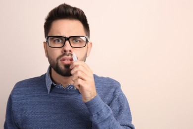 Man using nasal spray on beige background, space for text