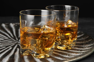 Photo of Whiskey and ice cubes in glasses on black table, closeup