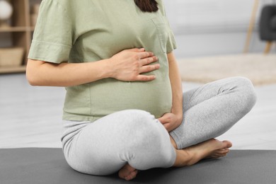 Pregnant woman sitting on yoga mat at home, closeup