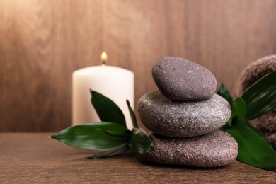 Photo of Stacked spa stones, bamboo leaves and candle on wooden table. Space for text