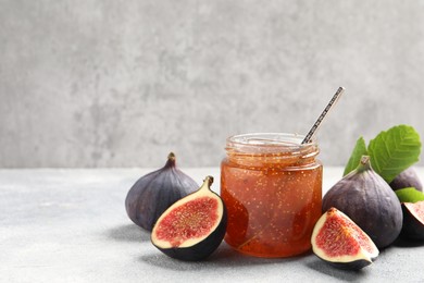 Photo of Glass jar with tasty sweet jam, green leaf and fresh figs on light grey table. Space for text