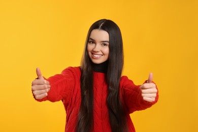 Teenage girl showing thumbs up on yellow background