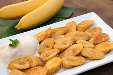 Photo of Tasty deep fried banana slices with ice cream and mint on wooden table, closeup