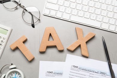 Photo of Word Tax made of wooden letters, documents, computer keyboard and glasses on grey table, flat lay