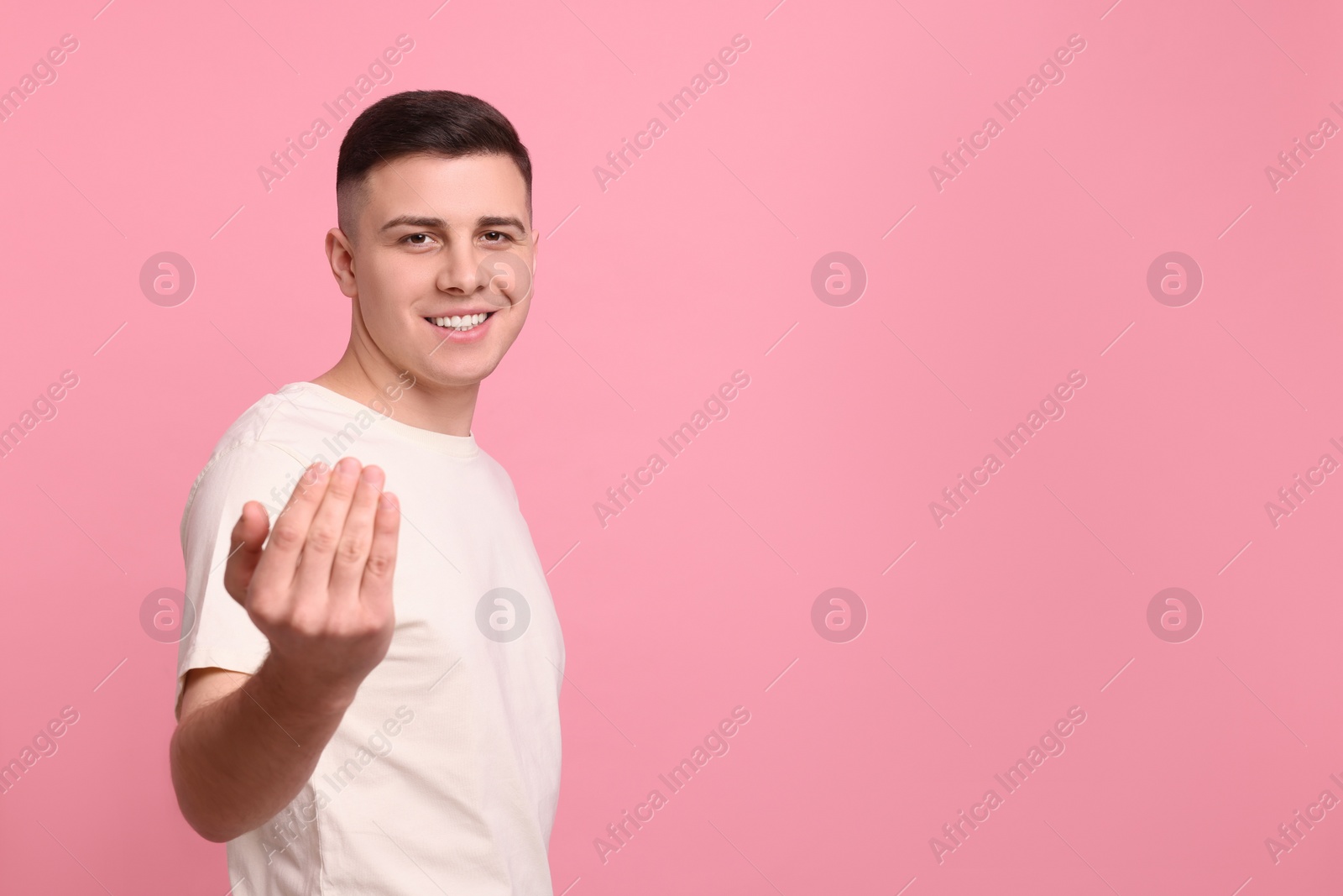 Photo of Handsome man inviting to come in against pink background. Space for text