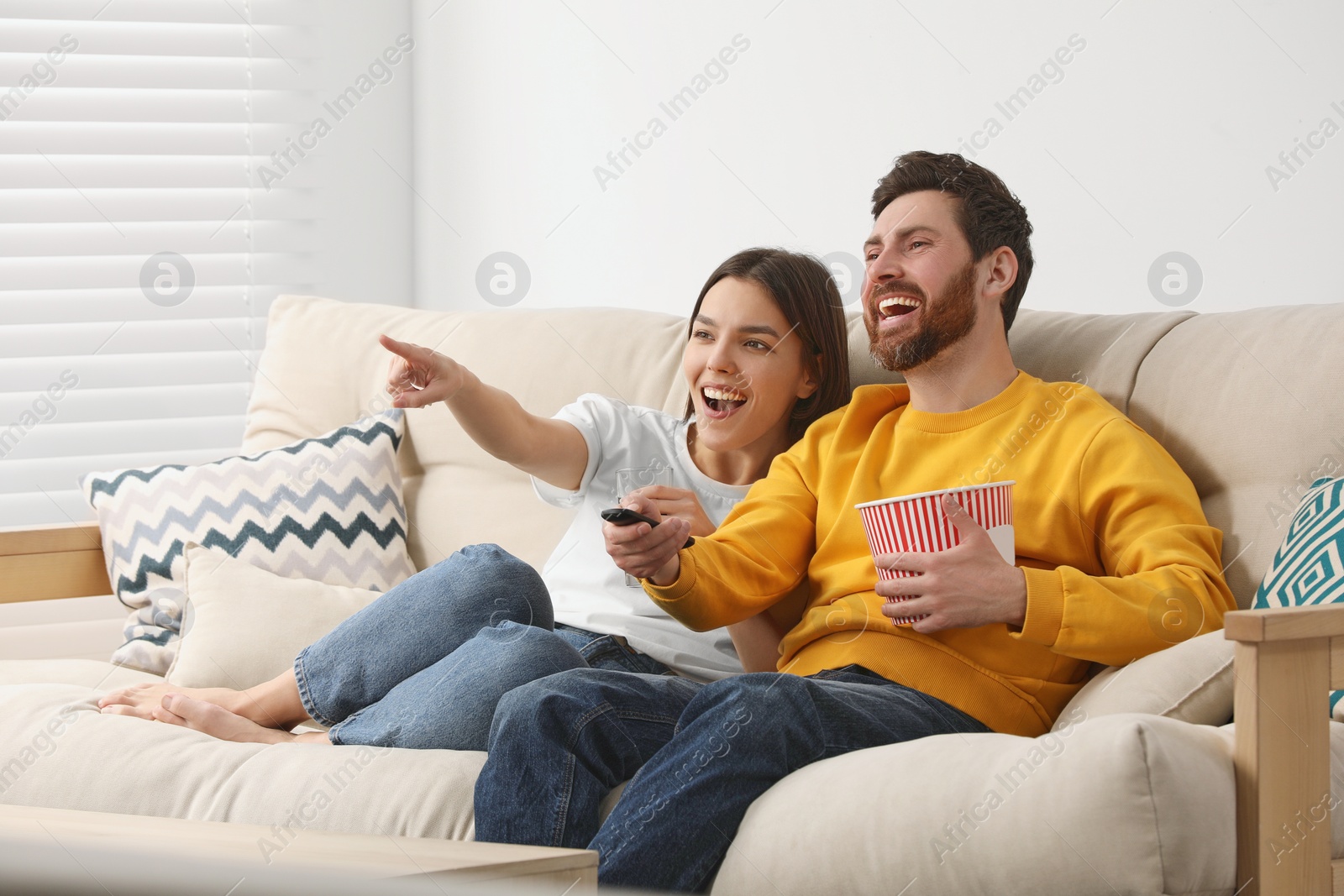 Photo of Happy couple watching TV with popcorn on sofa at home