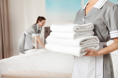 Photo of Chambermaid with stack of fresh towels in hotel room, closeup. Space for text