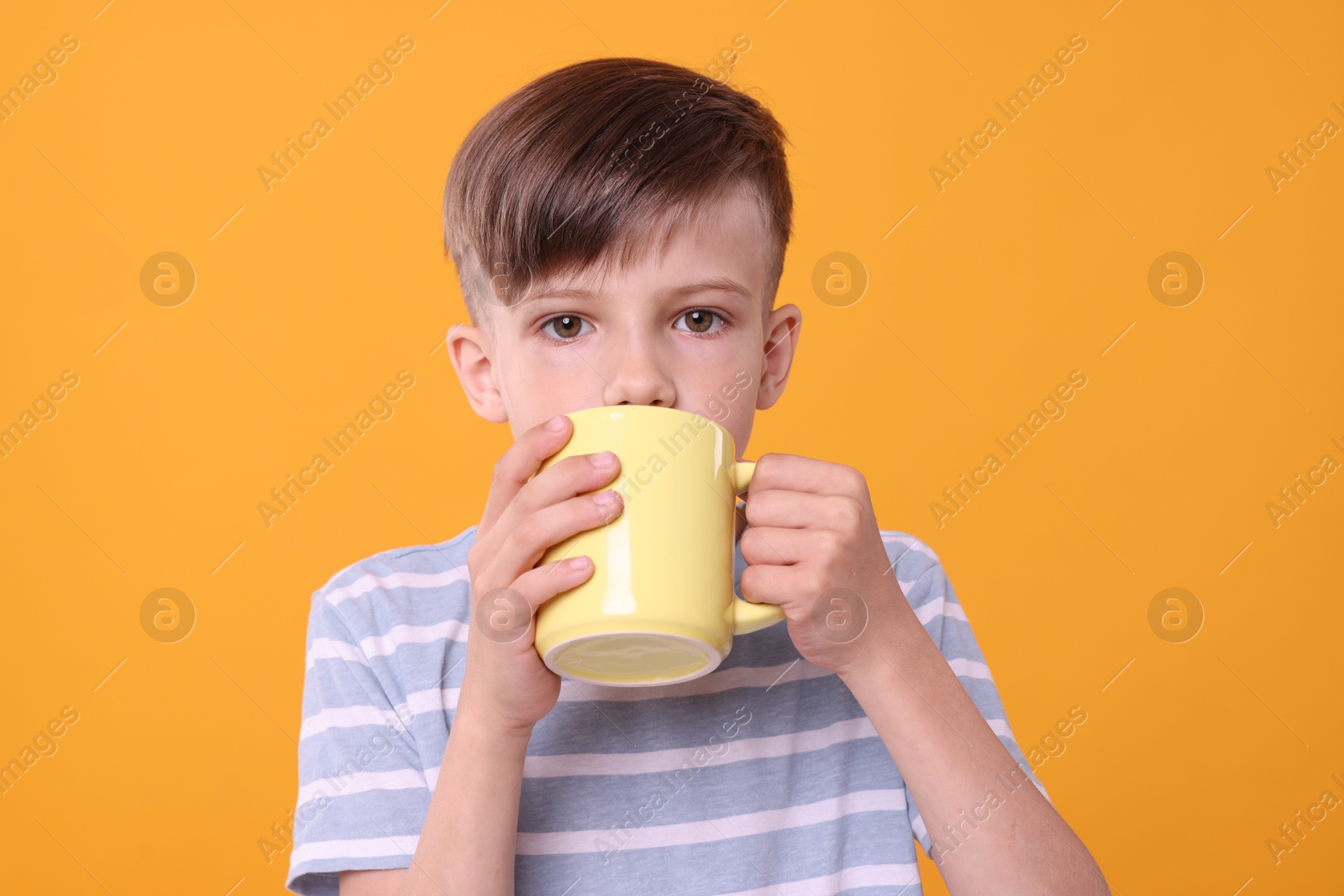 Photo of Cute boy drinking beverage from yellow ceramic mug on orange background