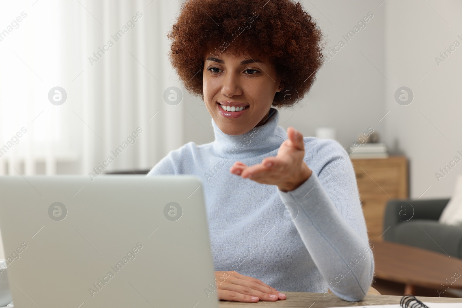 Photo of Beautiful young woman having video chat via laptop at wooden desk in room