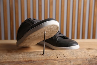 Photo of Metal nail in wooden plank and shoes on table