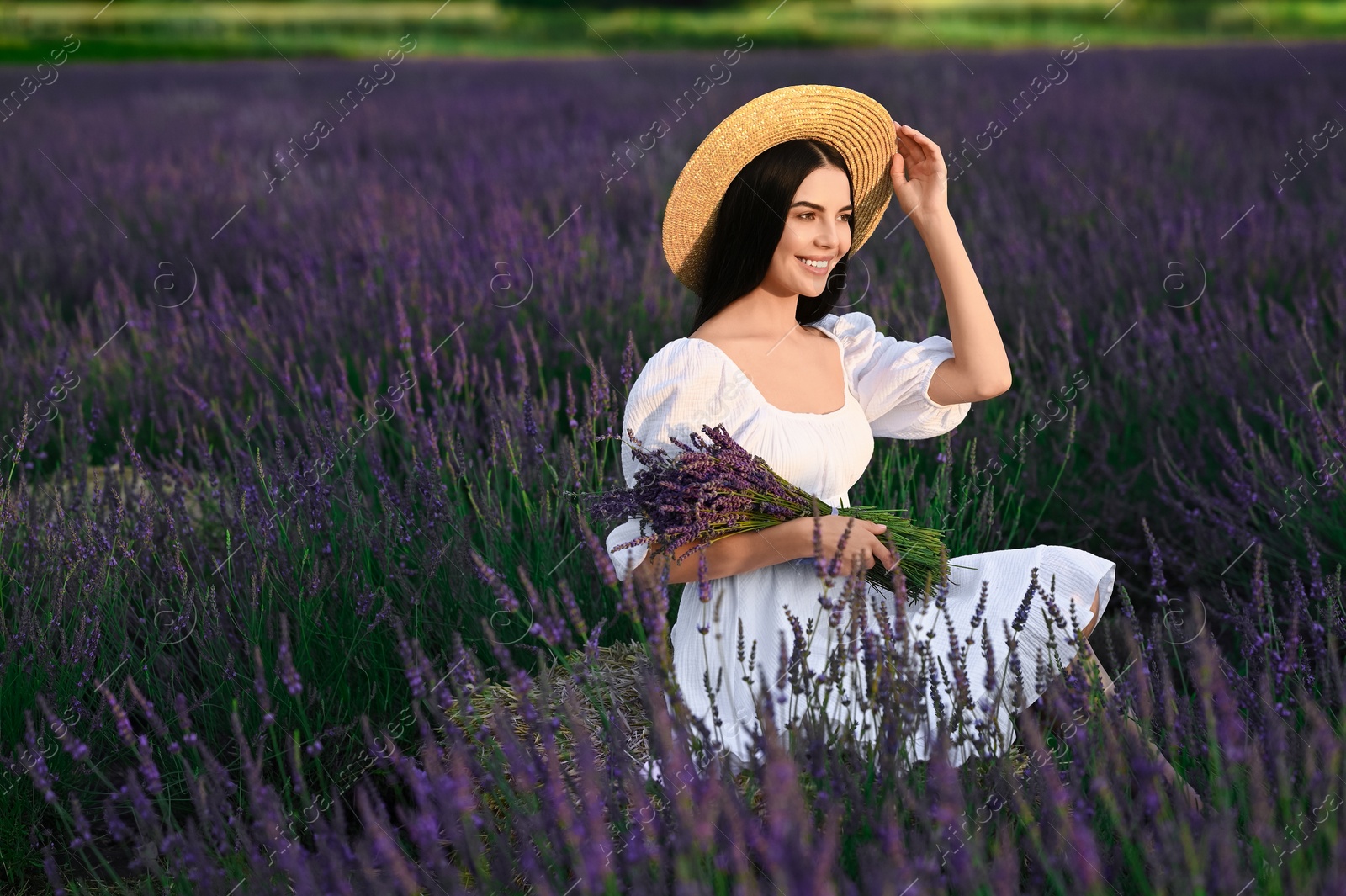 Photo of Beautiful young woman with bouquet sitting in lavender field