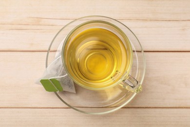 Tea bag and glass cup on light wooden table, top view