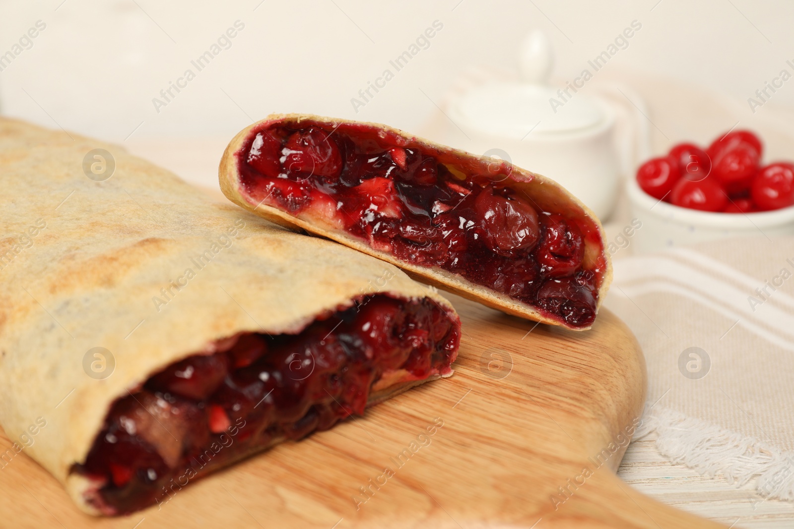 Photo of Delicious strudel with cherries on wooden board, closeup