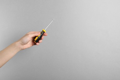 Photo of Woman holding screwdriver on grey background, closeup. Space for text