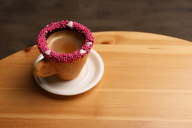 Delicious edible biscuit cup of coffee decorated with sprinkles on wooden table. Space for text
