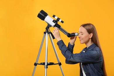 Young astronomer looking at stars through telescope on orange background, space for text