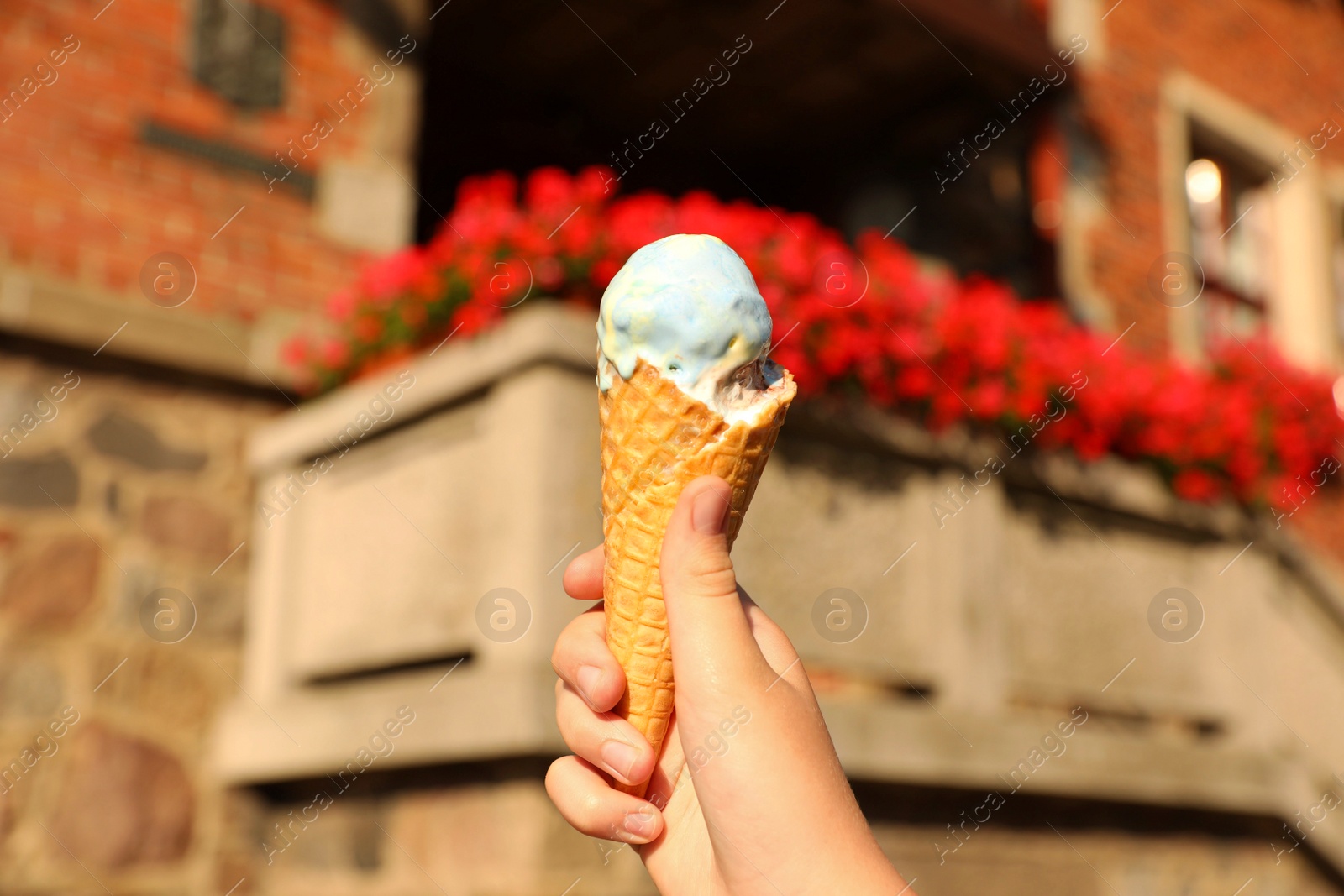 Photo of Woman holding delicious ice cream in wafer cone in city, closeup