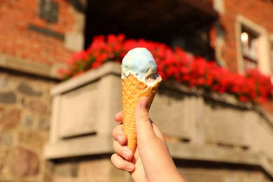 Photo of Woman holding delicious ice cream in wafer cone in city, closeup