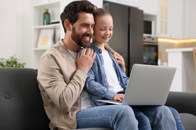 Happy man and his daughter with laptop on sofa at home