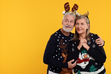 Photo of Senior couple in Christmas sweaters and reindeer headbands on orange background. Space for text