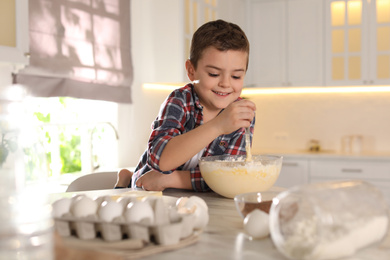 Cute little boy cooking dough in kitchen at home