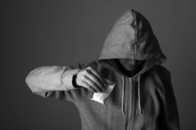 Drug dealer holding bag with cocaine on dark background, closeup. Black and white effect