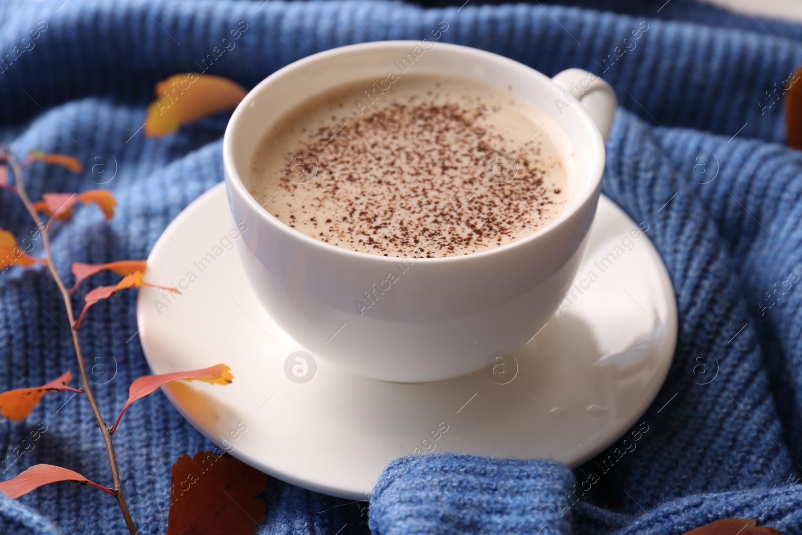 Photo of Cup of hot drink and leaves on blue knitted sweater, closeup. Cozy autumn atmosphere