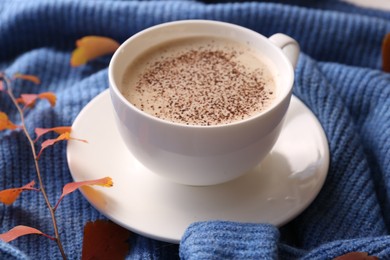 Cup of hot drink and leaves on blue knitted sweater, closeup. Cozy autumn atmosphere