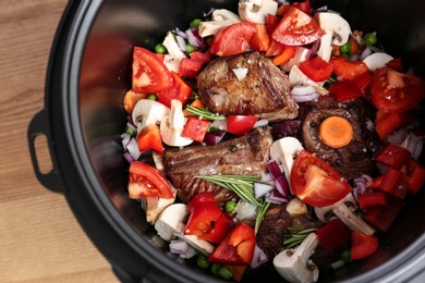 Photo of Delicious pork ribs with vegetables in multi cooker on table, closeup