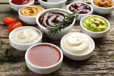 Photo of Different tasty sauces in bowls, rosemary and thyme on wooden table, closeup
