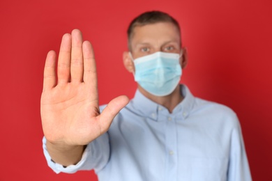 Photo of Man in protective mask showing stop gesture on red background. Prevent spreading of coronavirus