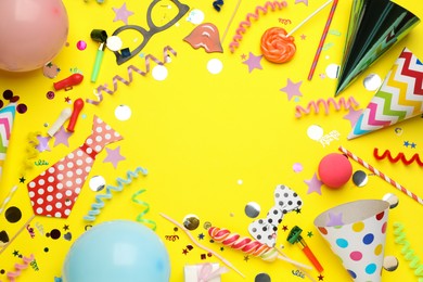Photo of Frame of party hats and other festive items on yellow background, flat lay with space for text. Birthday surprise