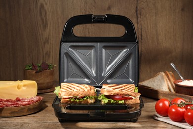 Photo of Modern grill maker with sandwiches and different products on wooden table