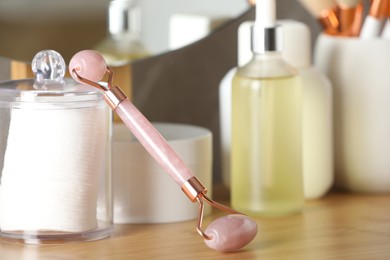 Natural face roller and cosmetic products on wooden table, closeup