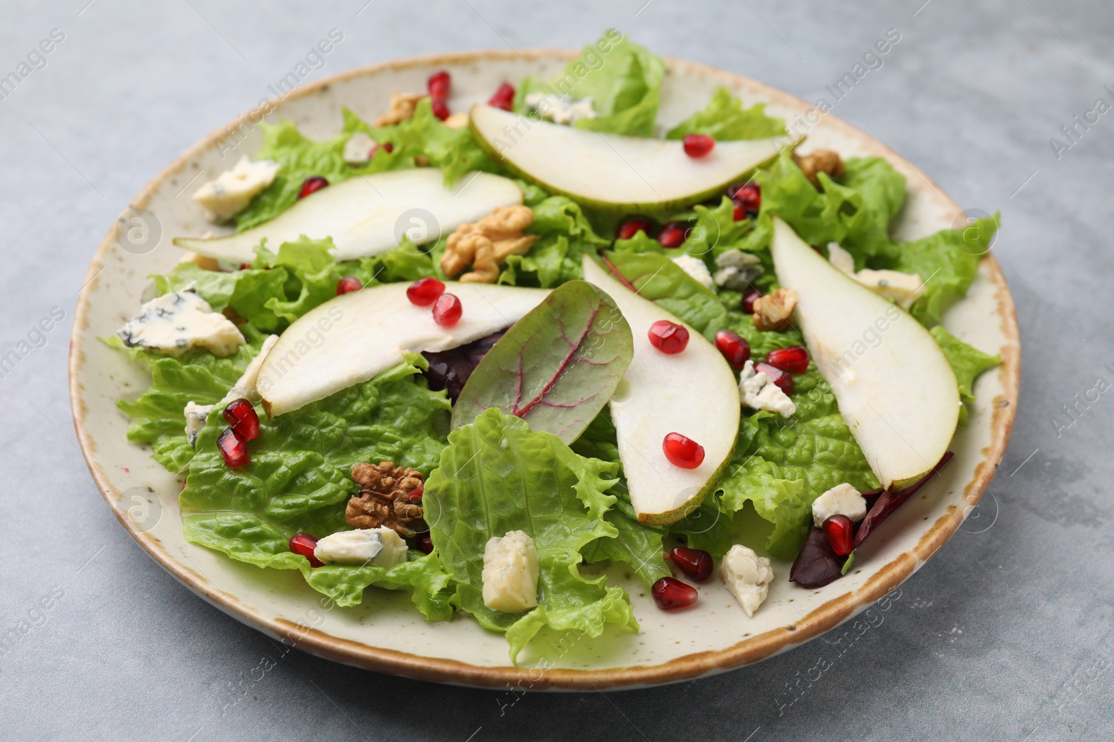 Photo of Plate with delicious pear salad on grey textured table, closeup