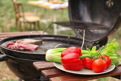 Photo of Plate with vegetables near barbecue grill outdoors