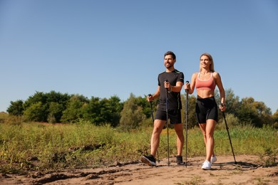 Photo of Happy couple practicing Nordic walking with poles outdoors on sunny day